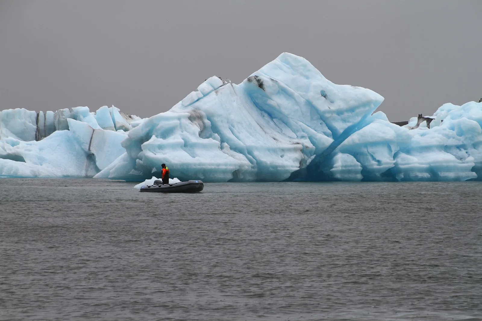 Ein Zodiac mit Guide fährt auf dem Jökulsárlón vor einem großen hellblauen Eisberg