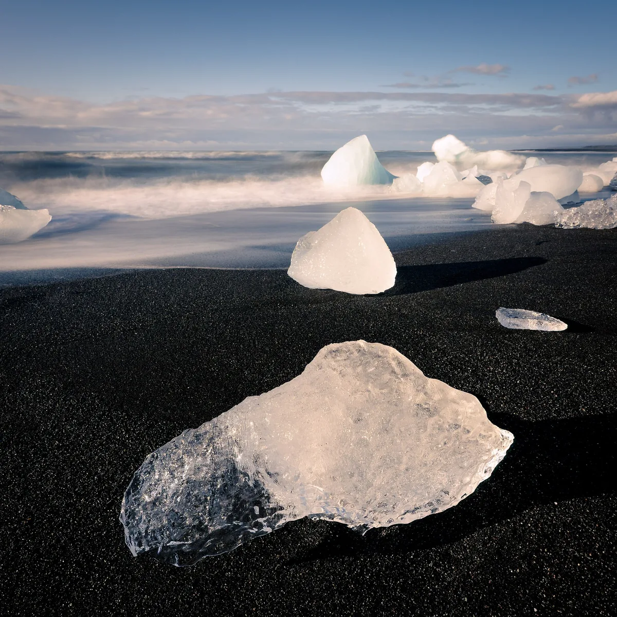 Klare Eisbrocken aus dem Jökulsárlón liegen am schwarzen Sandstrand der Fellsfjara im Gegenlicht
