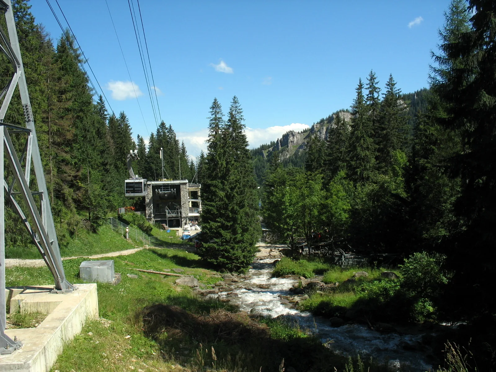 Die Talstation der Seilbahn auf den Kasprowy Wierch in Kuźnice am Bach Bystra, davor ein Mast der Bahn und Fichtenwald