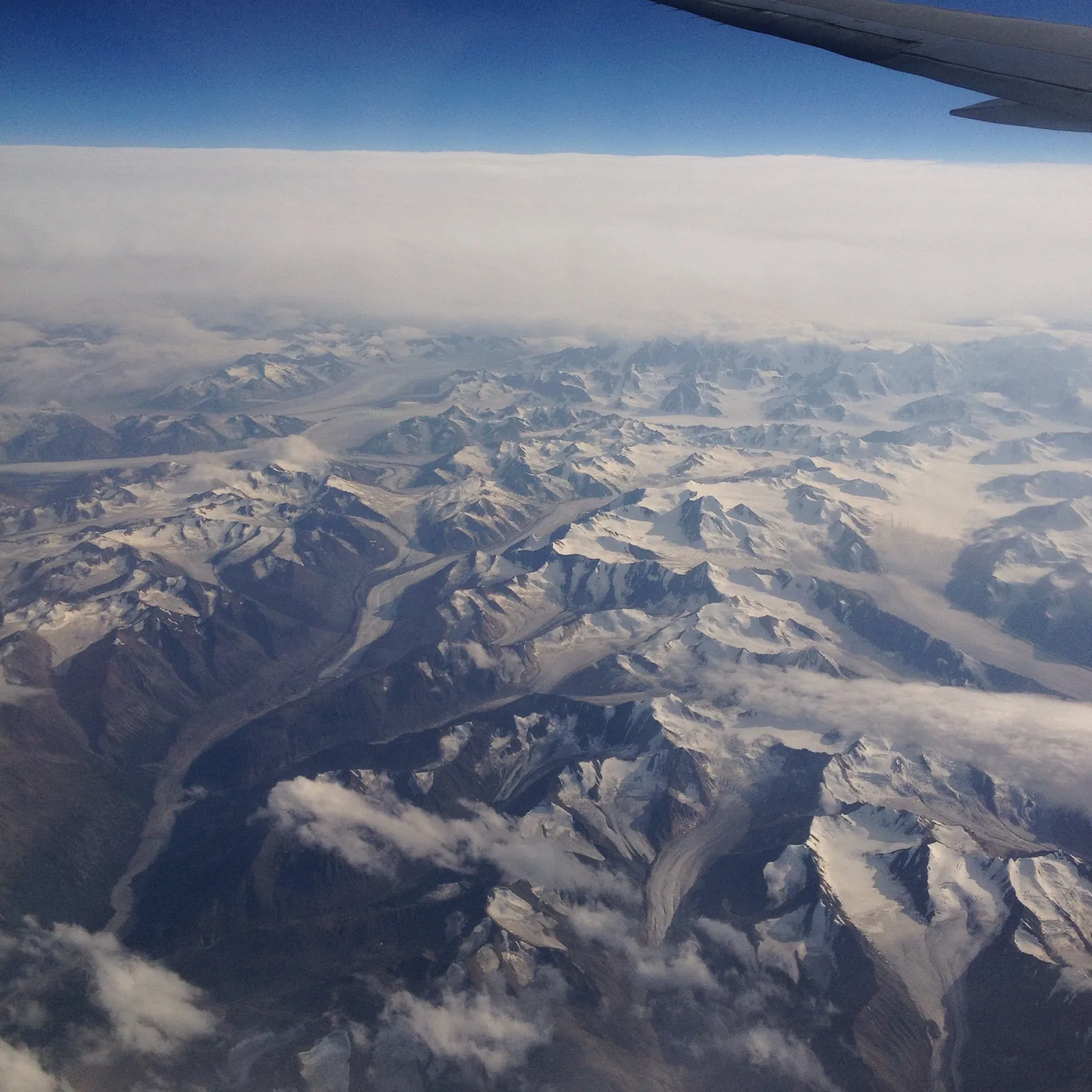 Blick aus dem Flugzeug über endlose schneebedeckte Bergketten und Gletscher, am oberen Bildrand die Tragfläche