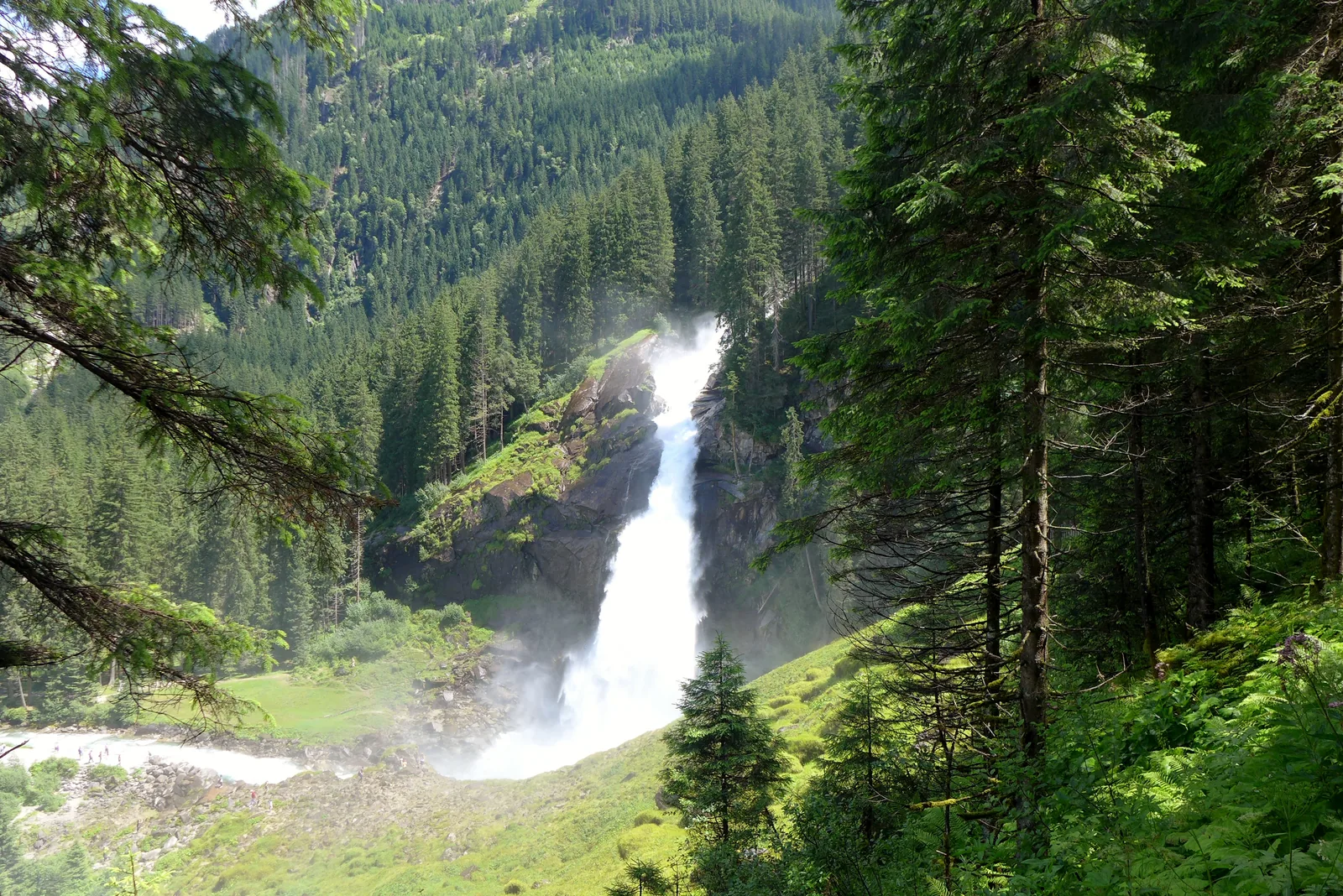 Die Krimmler Wasserfälle stürzen zwischen bewaldeten Hängen ins Tal, Blick vom Fuß der Fälle im Nationalpark Hohe Tauern