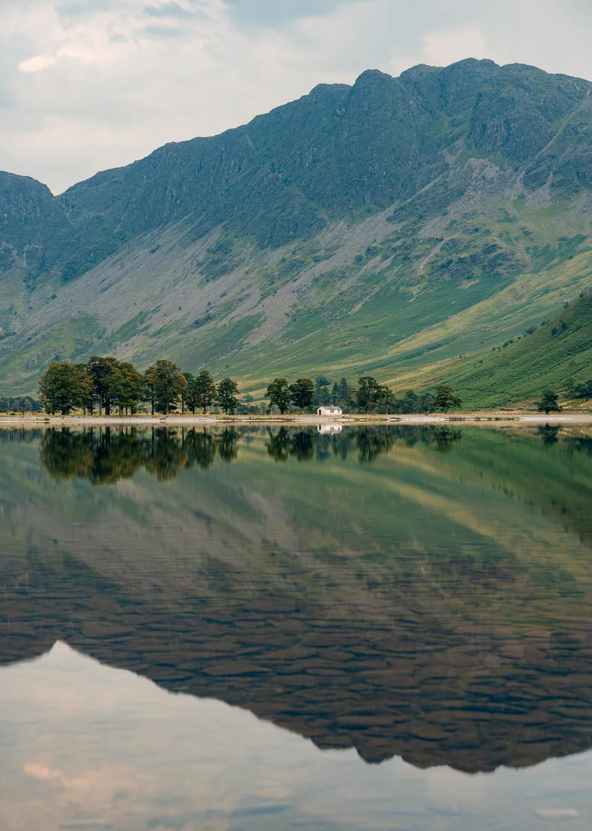 Der See Buttermere im Lake-District-Nationalpark mit steilen grünen Hängen, die sich im Wasser spiegeln