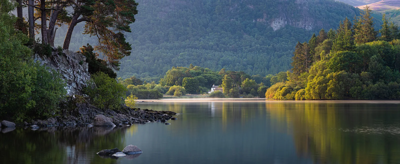 Kiefern und bewaldete Hänge spiegeln sich im ruhigen Derwentwater bei Friar’s Crag im Lake-District-Nationalpark