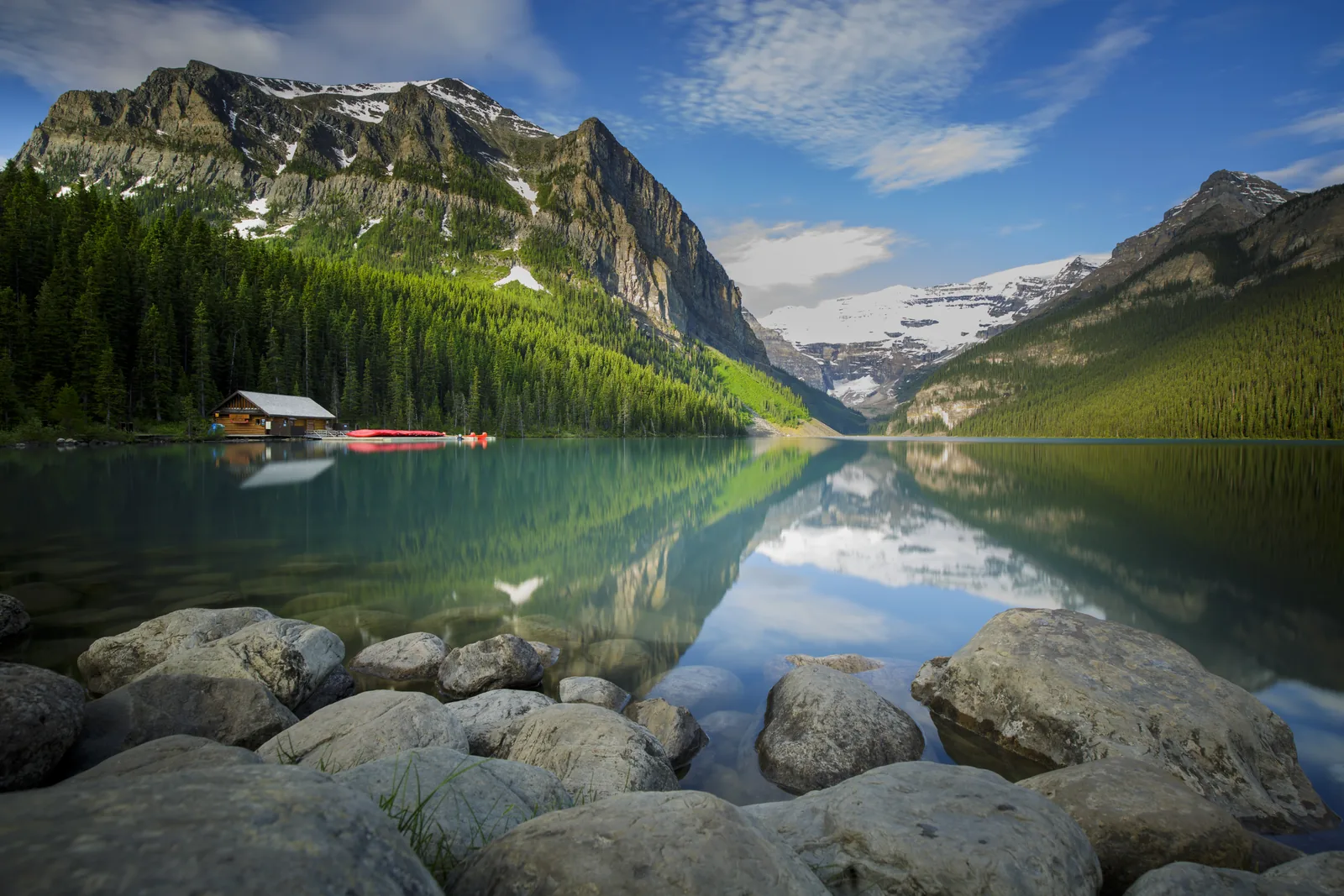 Lake Louise mit Bootshaus und roten Kanus, dahinter der Victoria-Gletscher, im Vordergrund Uferfelsen
