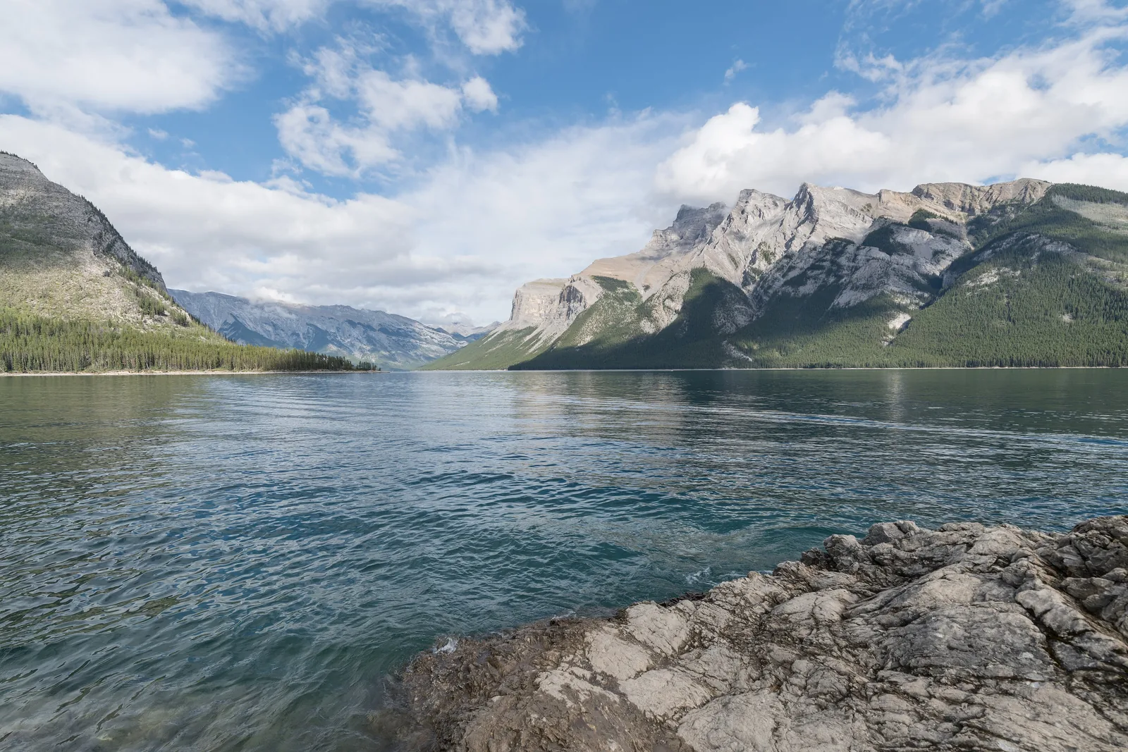 Lake Minnewanka im Banff-Nationalpark vom felsigen Westufer, rechts der Mount Inglismaldie, der See zieht sich weit ins Tal.