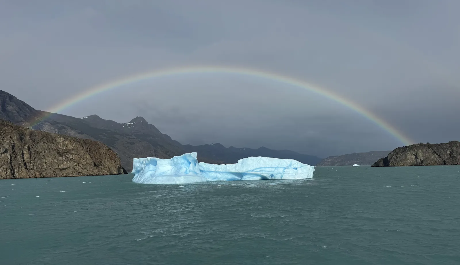 Ein Regenbogen spannt sich über einen blauen Eisberg auf dem Lago Argentino bei Puerto Bandera im Nationalpark Los Glaciares