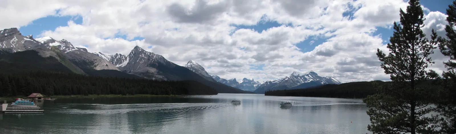 Panorama des Maligne Lake mit Bootshaus am Ufer und einer Bergkette unter Wolken