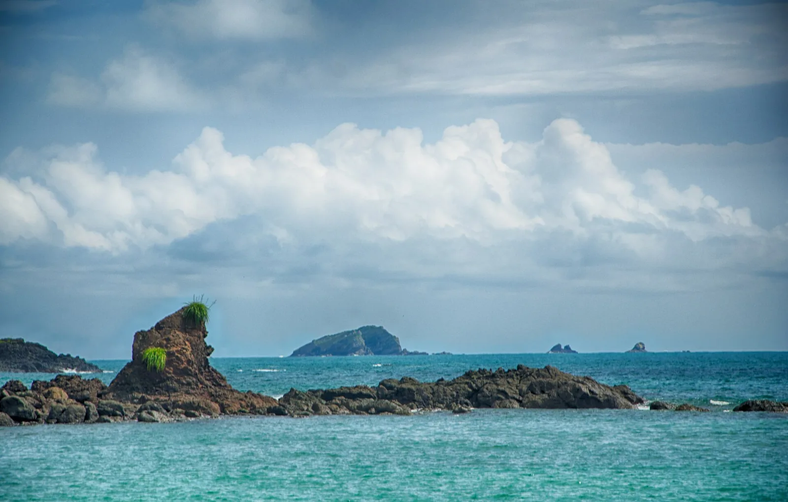 Sandstrand im Manuel-Antonio-Nationalpark mit dunklen Felsen, Wellen und bewaldeter Küste