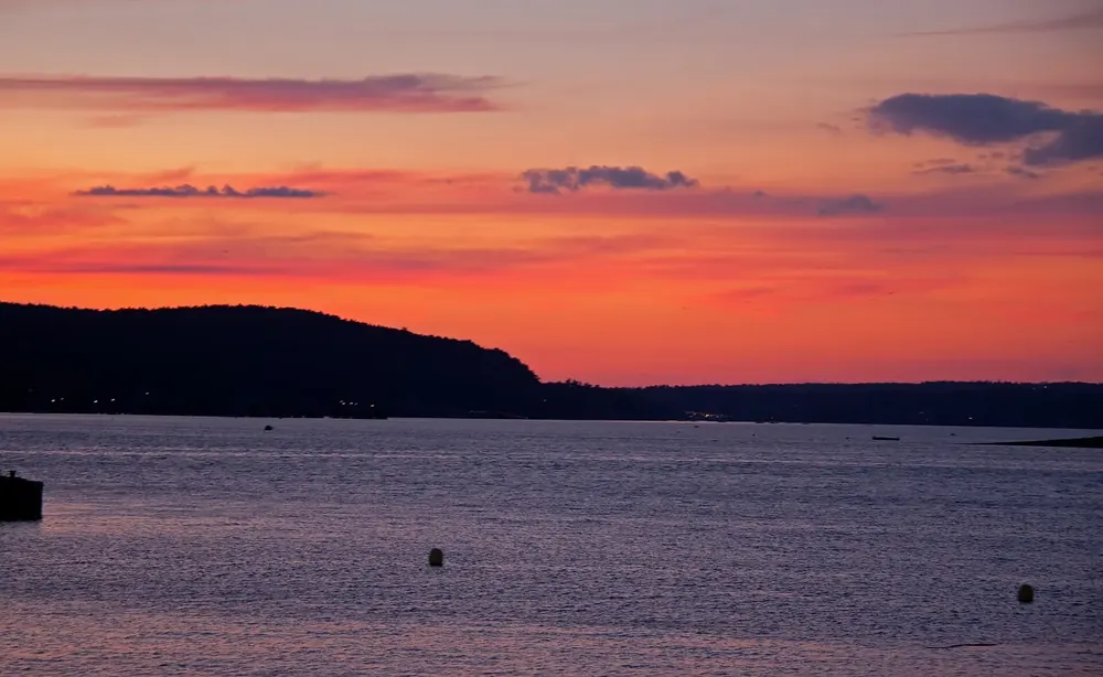Sonnenuntergang über dem Wasser vor Bar Harbor, dunkle bewaldete Inselsilhouetten unter orangerotem Abendhimmel