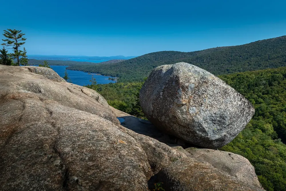 Bubble Rock: großer Granitfindling am Rand des South Bubble, dahinter ein langgestreckter See und bewaldete Hügel