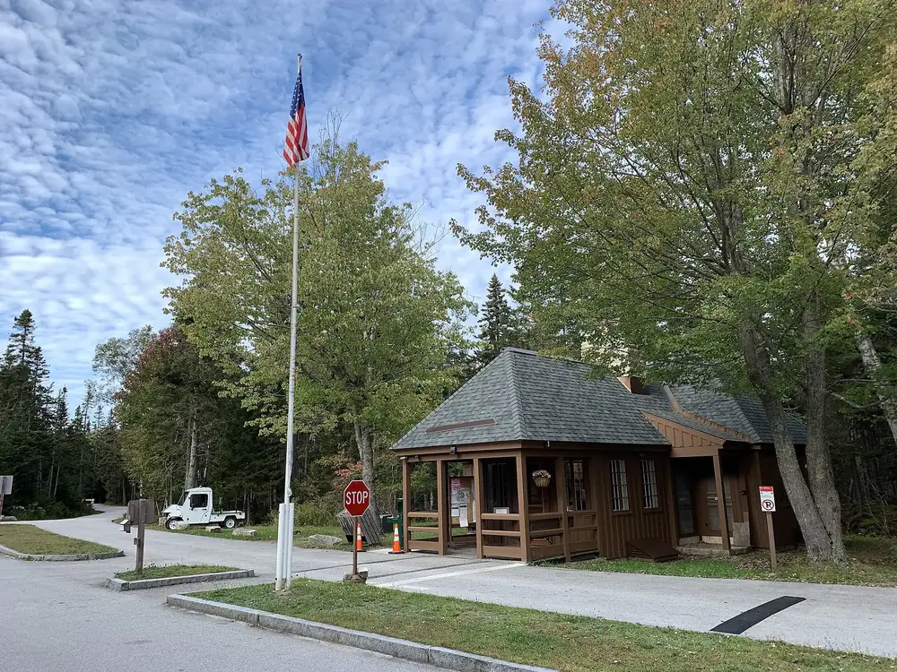Einfahrt zum Seawall Campground mit hölzernem Kassenhäuschen, Fahnenmast und hohen Laub- und Nadelbäumen