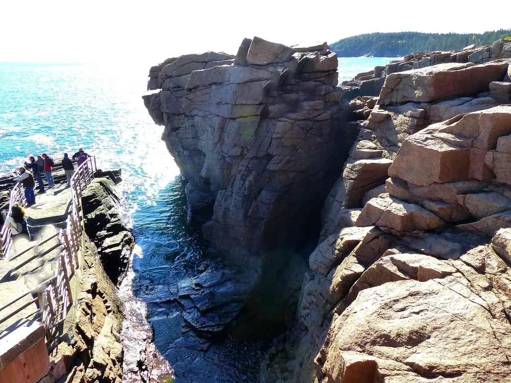 Thunder Hole: schmale Felsspalte im rosafarbenen Granit, links die Aussichtsplattform mit Geländer über der Brandung