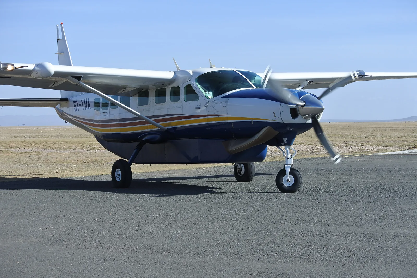 Ein einmotoriges Kleinflugzeug steht auf der asphaltierten Landepiste im Amboseli-Nationalpark, dahinter die flache, trockene Ebene