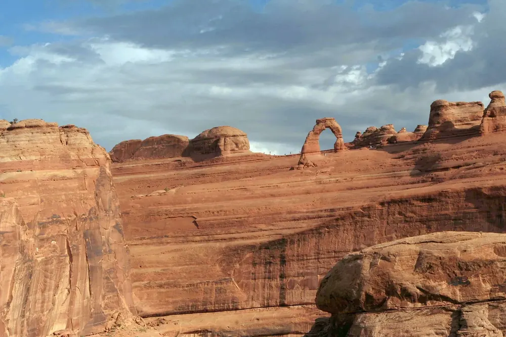 Blick vom Delicate Arch Viewpoint über eine Schlucht zum Delicate Arch auf dem roten Sandsteinrücken