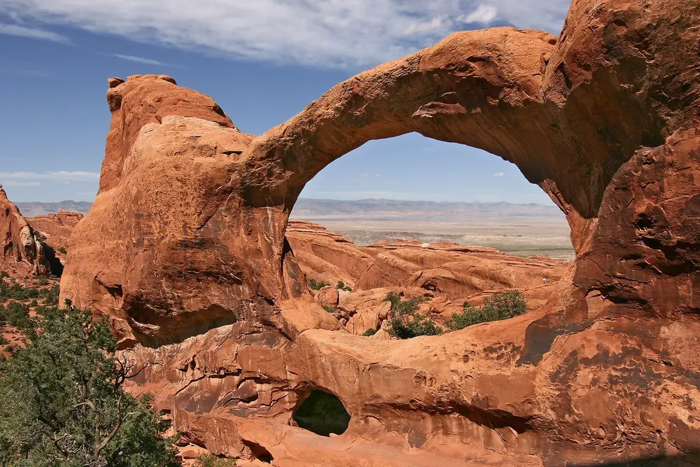 Double O Arch: großer ovaler Sandsteinbogen über einem kleineren Felsloch, Blick hindurch auf die weite Ebene