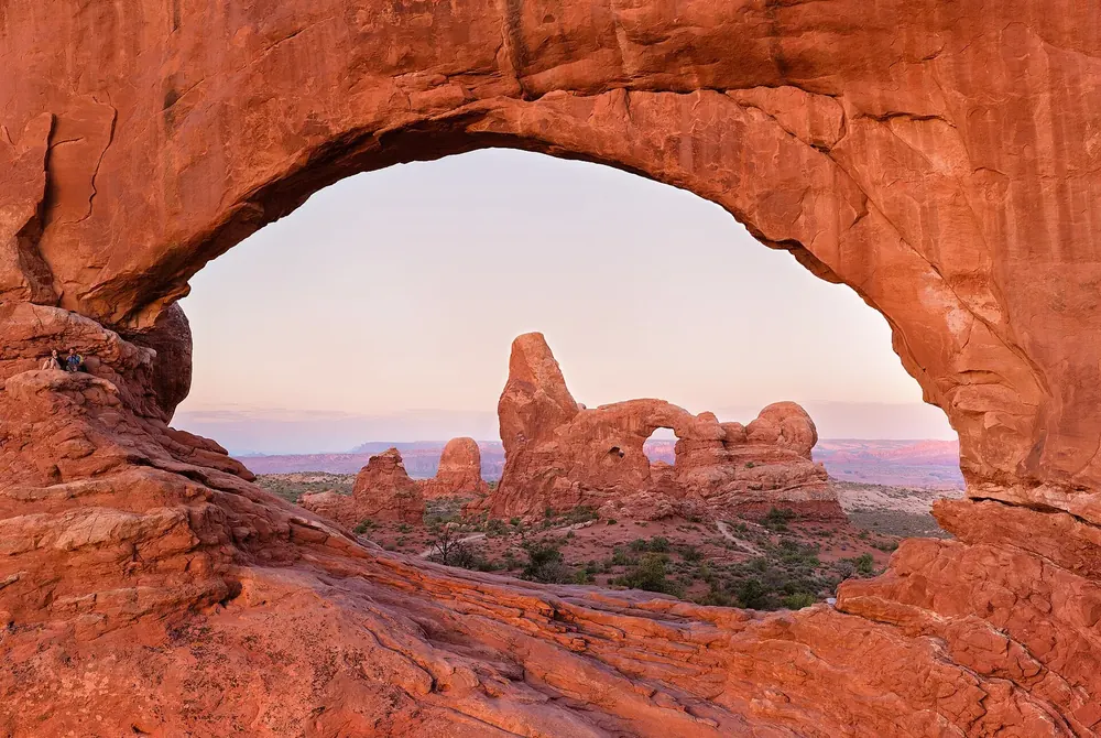 Blick durch den rot leuchtenden Felsbogen North Window auf den Turret Arch und die Ebene dahinter
