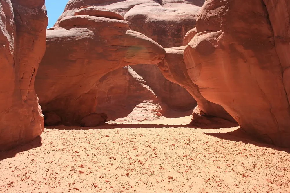 Sand Dune Arch: niedriger Sandsteinbogen zwischen engen roten Felswänden, darunter feiner rötlicher Sand