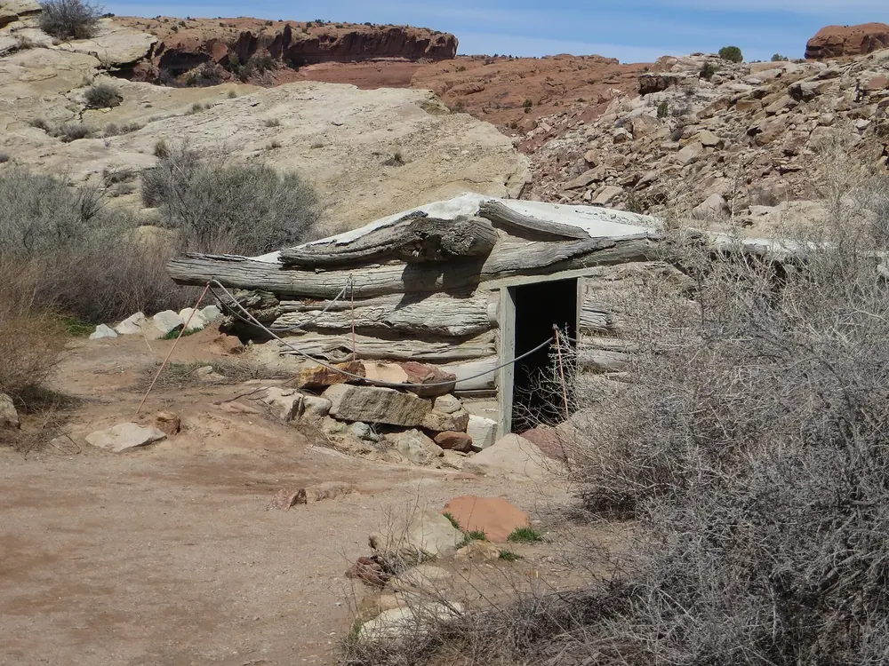 Historischer Erdkeller der Wolfe Ranch aus verwitterten Holzbalken, eingebettet in einen Hang zwischen Wüstensträuchern