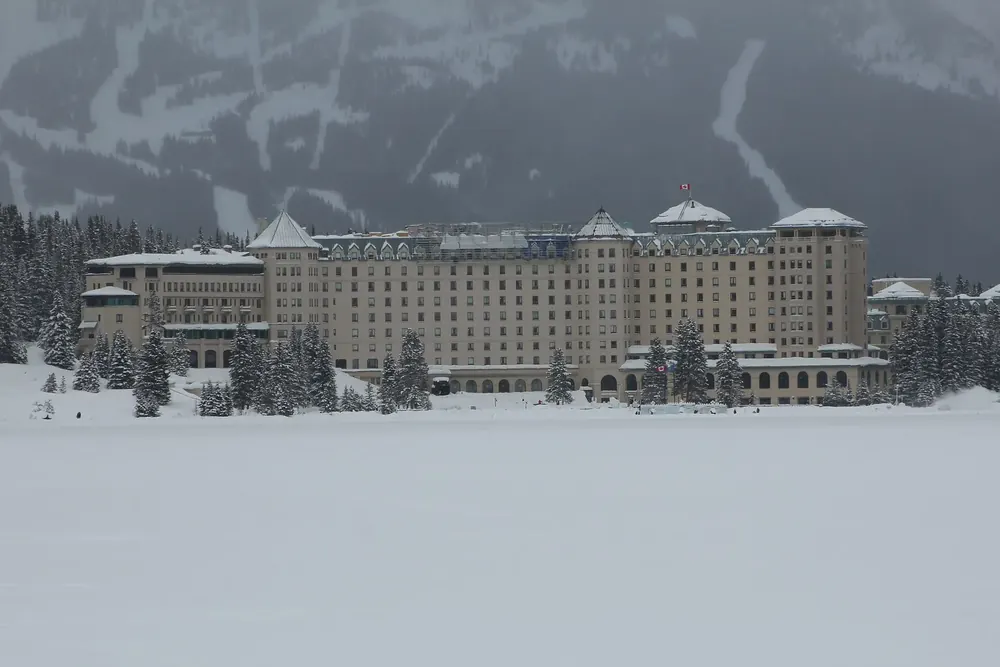 Hotel Fairmont Château Lake Louise im Winter, davor der zugefrorene verschneite See und verschneiter Nadelwald