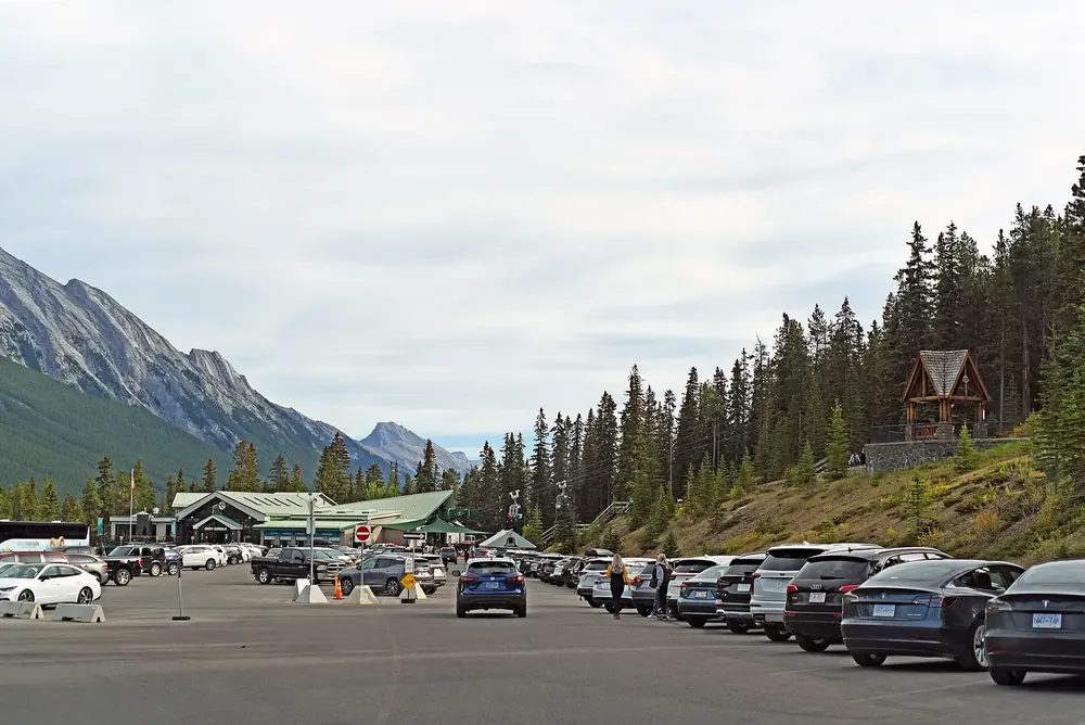 Parkplatz an der Talstation der Banff Gondola, gesäumt von Nadelwald, dahinter steile graue Berghänge