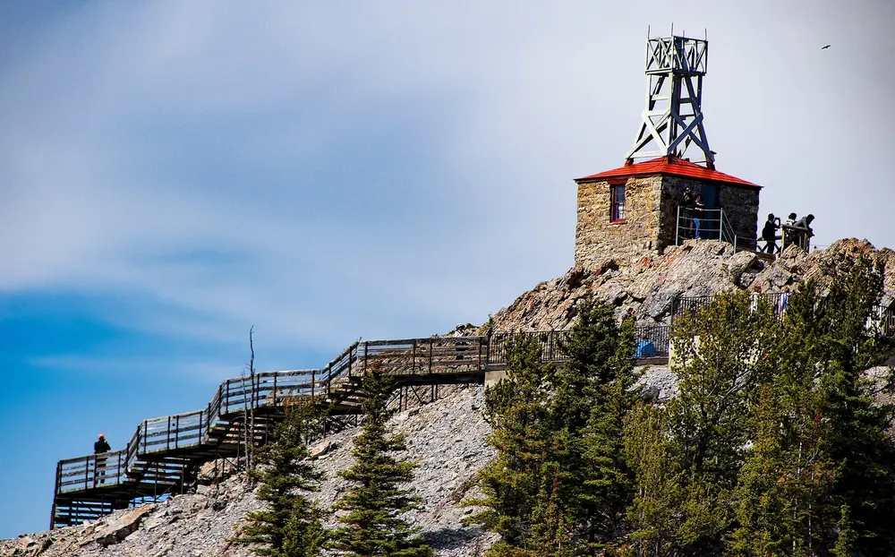 Historische Wetterstation aus Stein auf dem Sanson Peak, davor hölzerne Treppen und Stege am felsigen Gipfel