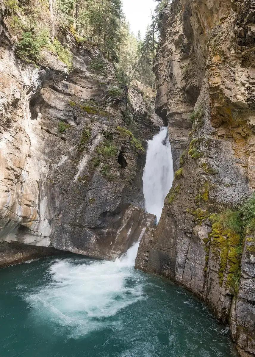 Lower Falls im Johnston Canyon: Wasserfall stürzt durch eine enge Kalksteinschlucht in ein türkisfarbenes Becken