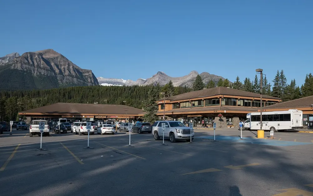 Samson Mall im Ort Lake Louise neben dem Besucherzentrum: Holzbauten, Parkplatz und Shuttlebus vor Bergen