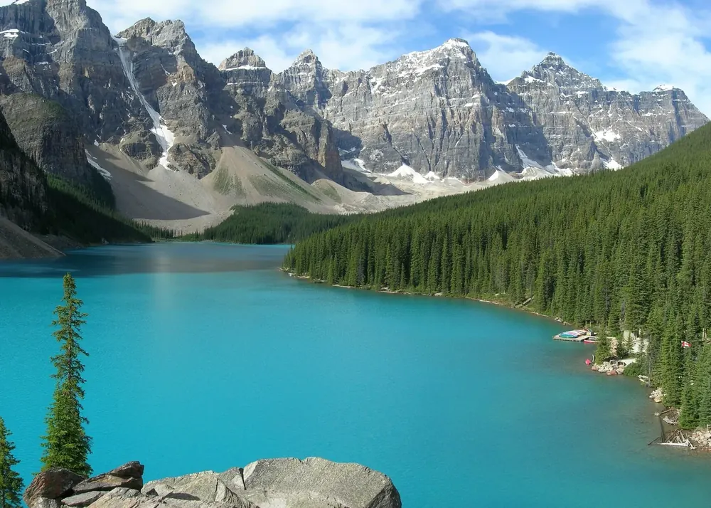 Türkisfarbener Moraine Lake vom Aussichtspunkt am Nordufer, dahinter eine Kette schroffer, teils verschneiter Gipfel