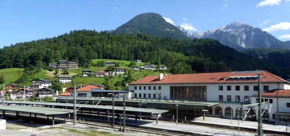 Hauptbahnhof Berchtesgaden von Nordwesten: Bahnsteige und Empfangsgebäude, dahinter bewaldete Hänge und Gipfel