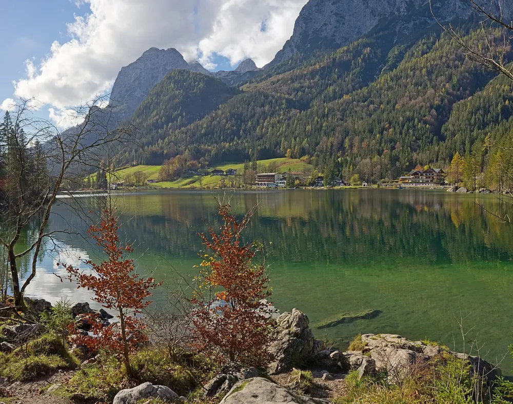 Hintersee mit klarem grünem Wasser und Herbstlaub am Ufer, dahinter die Felswände der Reiter Alpe