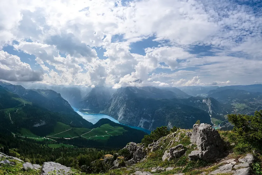 Blick vom Gipfel des Jenner über Felsen und Almflächen hinab auf den Königssee zwischen steilen Bergflanken