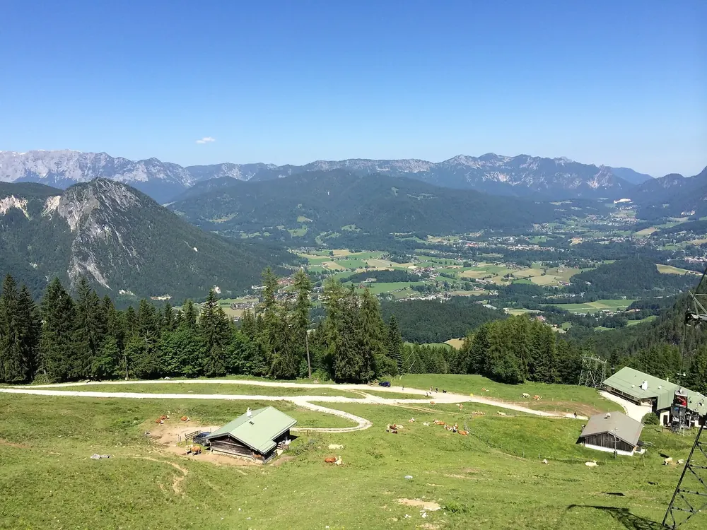 Aussicht an der Mittelstation der Jennerbahn: Almwiese mit Gebäuden, dahinter das Berchtesgadener Tal und Bergketten