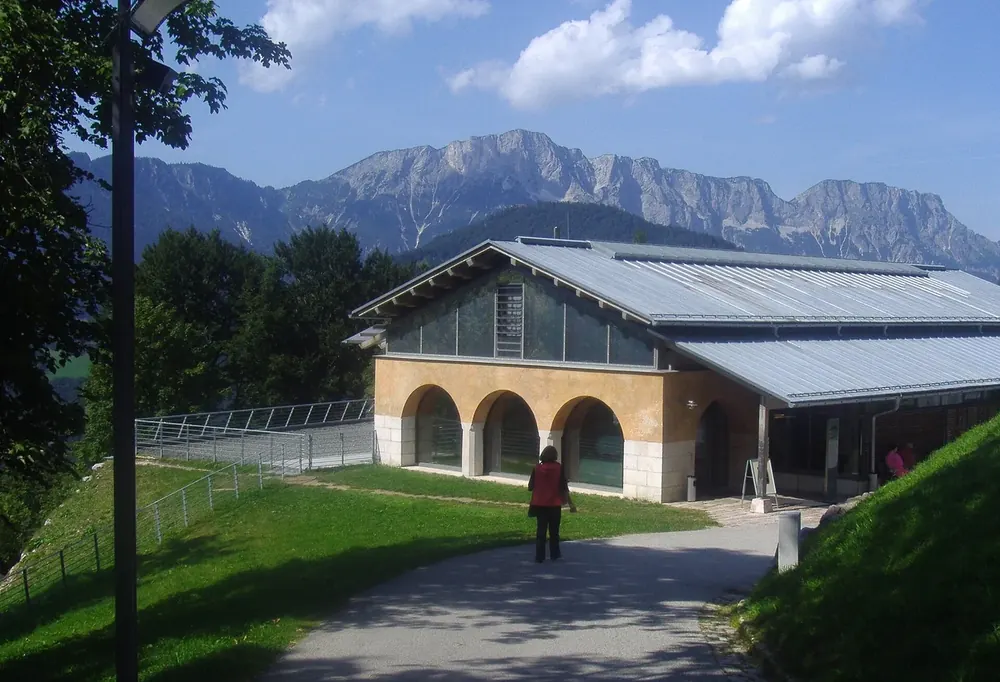 Dokumentationszentrum Obersalzberg: flacher Bau mit Rundbögen auf einer Wiese, dahinter das Untersberg-Massiv