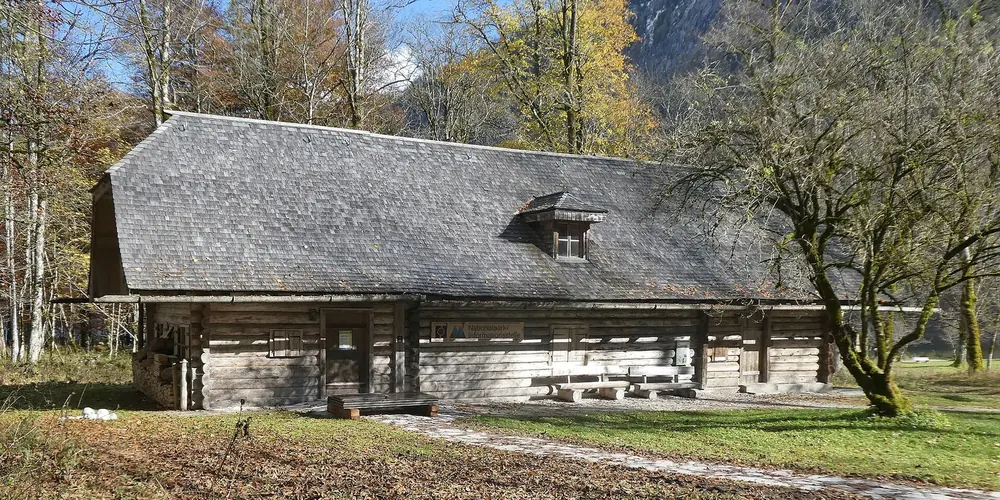 Nationalpark-Informationsstelle St. Bartholomä: langgestrecktes historisches Holzgebäude mit steilem Schindeldach zwischen Bäumen