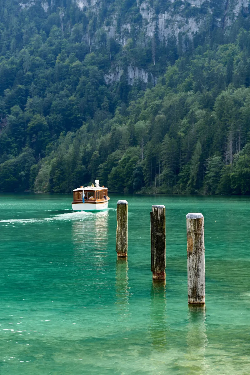 Ausflugsboot auf dem smaragdgrünen Königssee bei der Seelände in Schönau, vorn alte Holzpfähle im Wasser