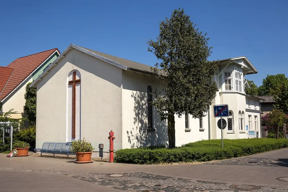 Katholische Kirche St. Michael in Zingst: weißer Bau mit rotem Kreuz, daneben eine Villa und ein Baum