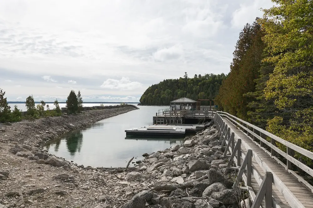 Bootsanleger von Flowerpot Island: Holzsteg und Kiesufer an einer ruhigen Bucht, dahinter bewaldete Felsküste