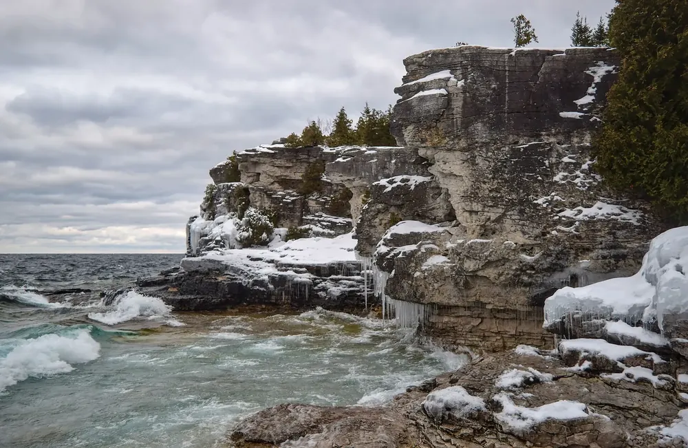 Kalksteinklippen der Indian Head Cove im Winter, Eis an den Felsen und schäumende Brandung am Ufer