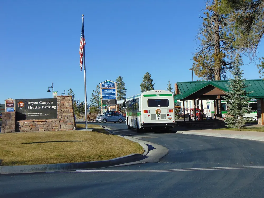 Haltestelle des Bryce-Canyon-Shuttles in Bryce Canyon City: Shuttlebus, Wartehäuschen, Fahnenmast und Kiefern