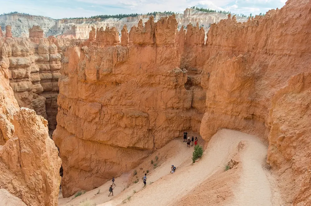 Wall Street im Navajo Loop von oben: enge Schlucht zwischen hohen orangefarbenen Felswänden, unten Wanderer auf dem Weg