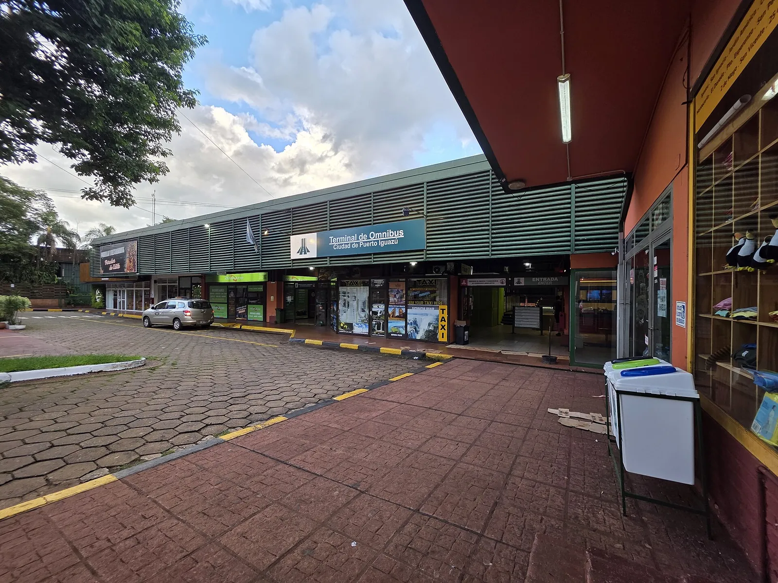 Busbahnhof Puerto Iguazú: lange Ladenzeile unter einem Vordach mit dem Schild „Terminal de Omnibus“, davor ein gepflasterter Vorplatz