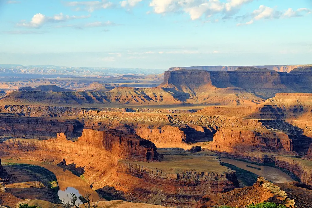 Blick vom Dead Horse Point auf eine tiefe Flussschleife zwischen rot leuchtenden Canyonwänden bei Sonnenaufgang