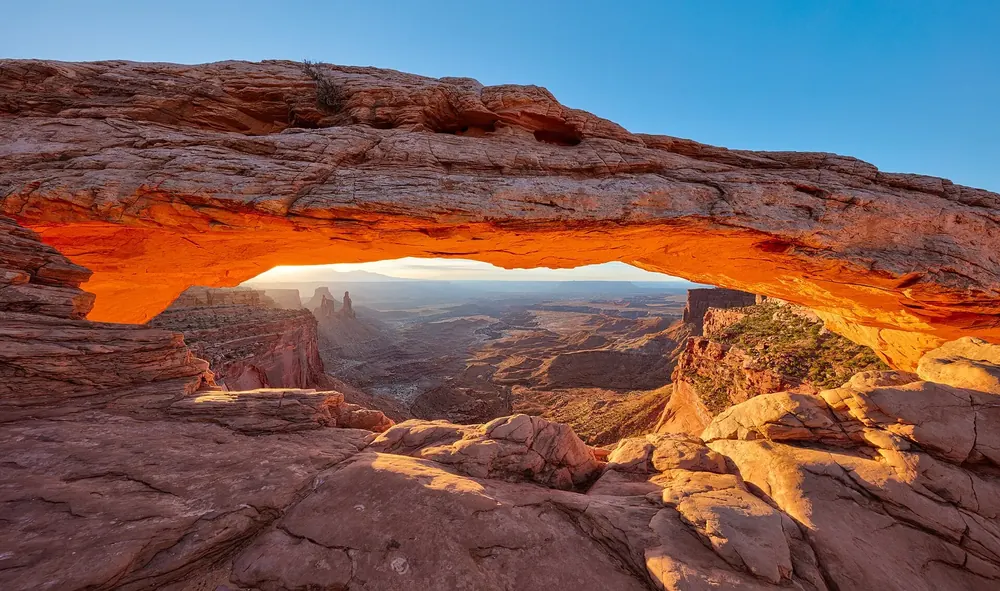 Mesa Arch bei Sonnenaufgang: die Unterseite des Felsbogens glüht orange, darunter der Blick in die Canyonlandschaft