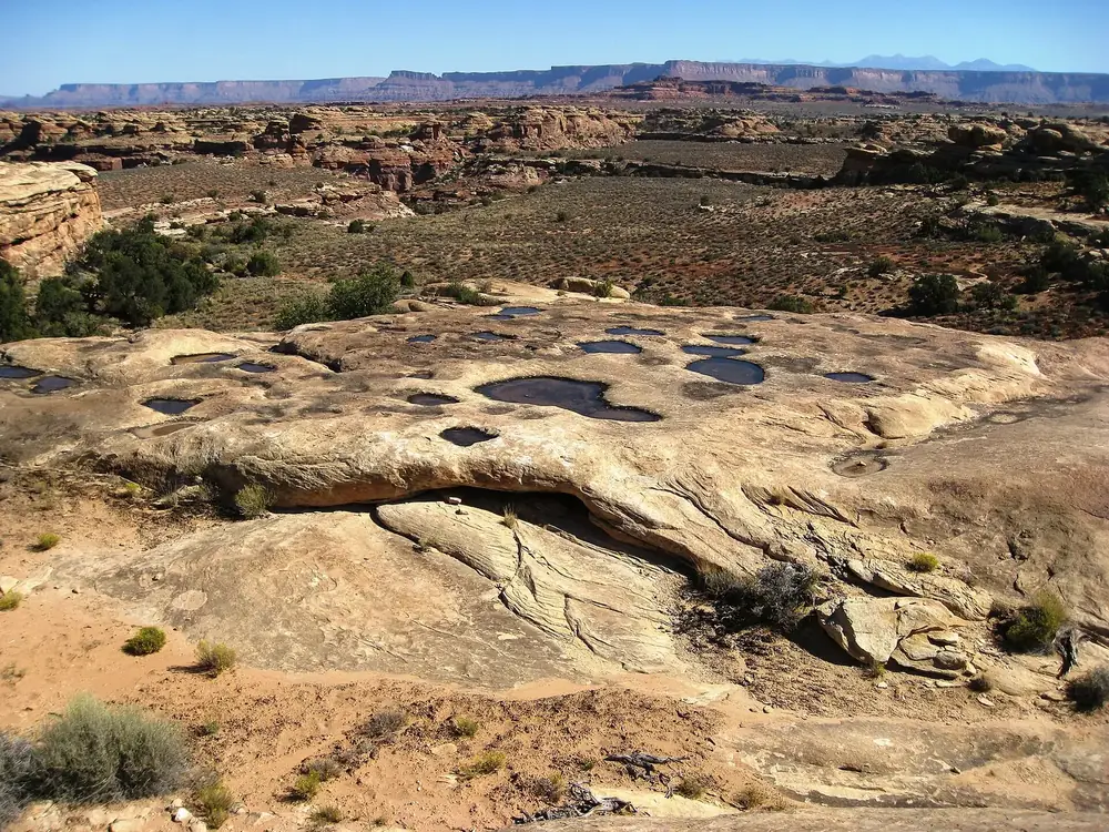 Pothole Point: mit Regenwasser gefüllte Mulden im hellen Sandstein, dahinter weite Canyonlandschaft und Tafelberge