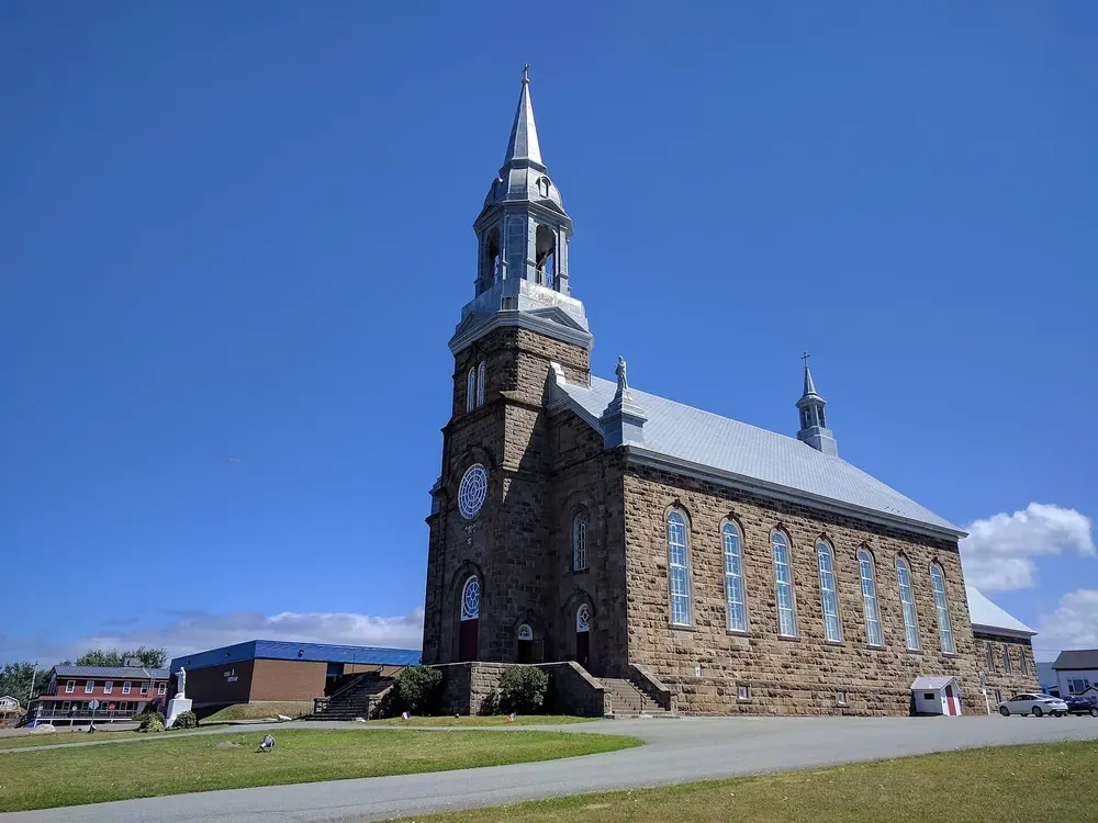 Große Steinkirche in Chéticamp mit hohem, spitzem Turm unter tiefblauem Himmel