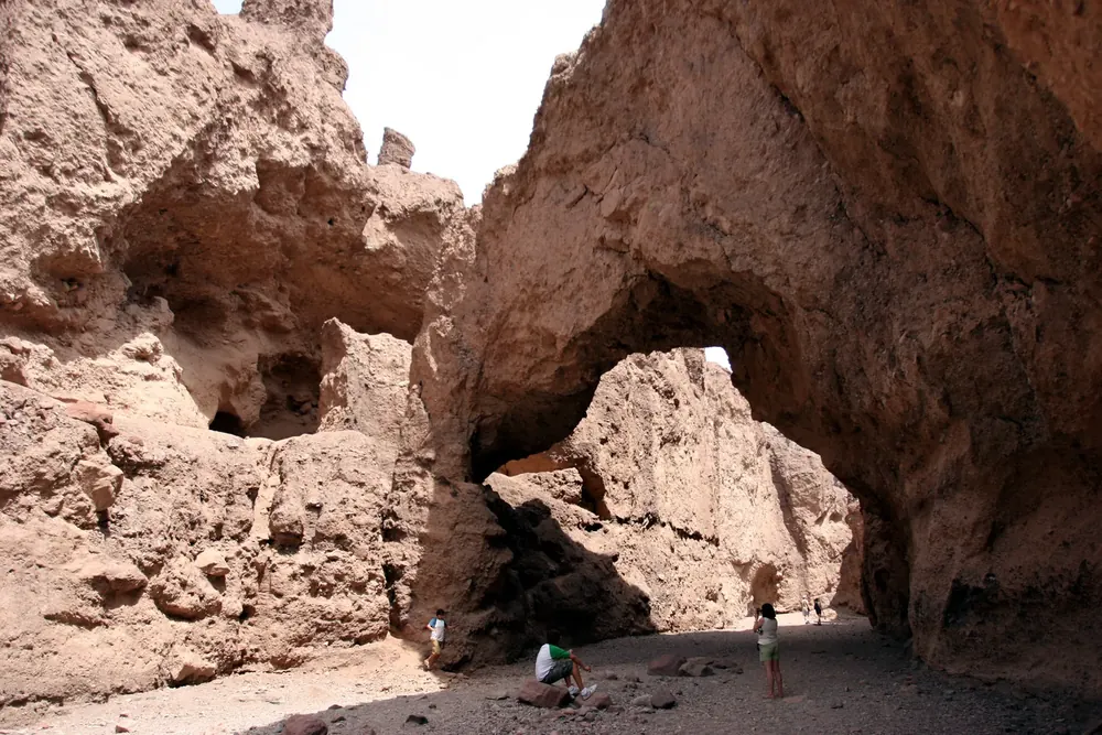 Natural Bridge: mächtige Felsbrücke über einer Schlucht aus hellbraunem Gestein, darunter kleine Wanderer