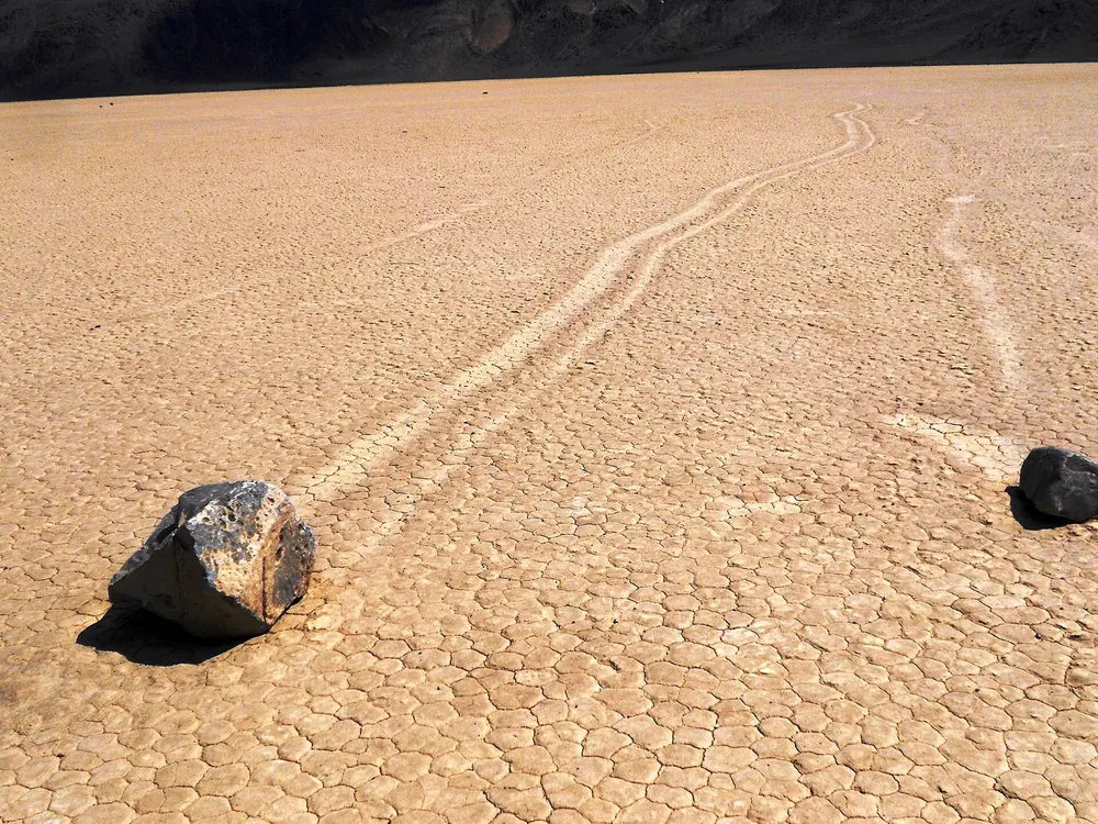 Racetrack Playa: dunkle Wandersteine mit langen Schleifspuren auf dem rissigen, ausgetrockneten Seeboden