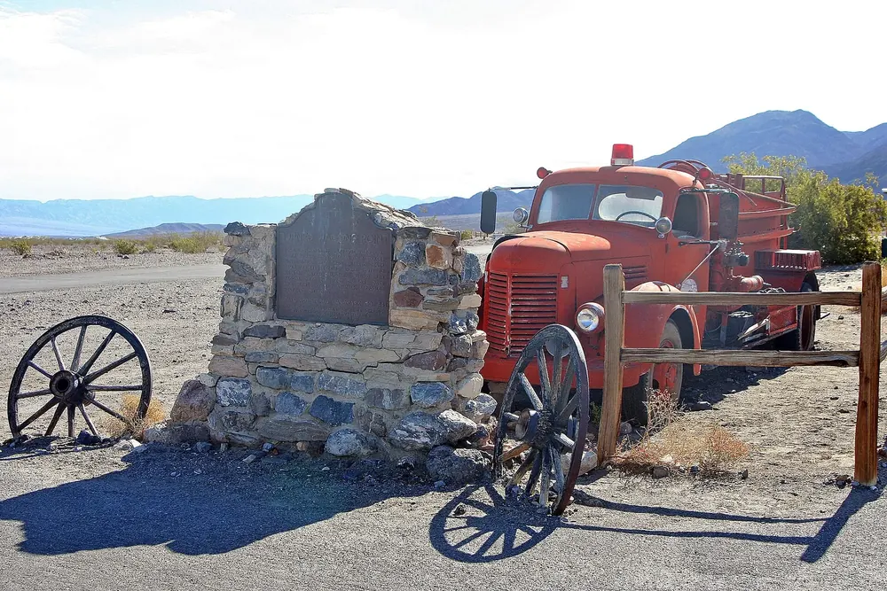 Stovepipe Wells: historischer Gedenkstein, altes rotes Feuerwehrauto und Wagenräder vor Wüstenbergen