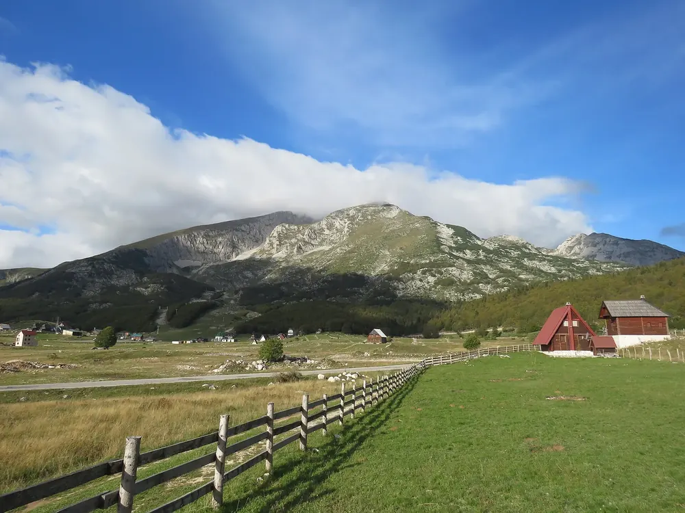 Savin Kuk über dem Weiler Motički Gaj: grüne Almwiesen, Holzzaun und rote Hütte vor dem Bergmassiv