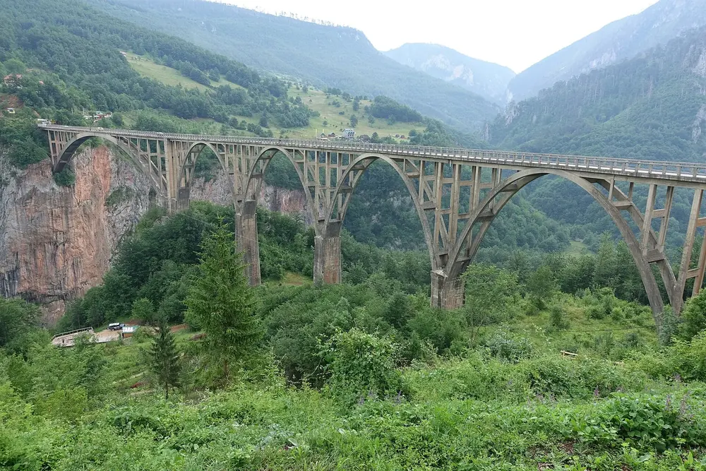 Đurđevića-Tara-Brücke: Betonbogenbrücke mit mehreren Bögen über der bewaldeten Tara-Schlucht vor grünen Berghängen